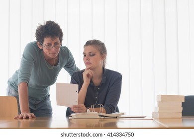 Librarian And Female Student Reading File Index Card At Library Desk