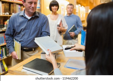 Librarian Handing Book To Man At Library Desk