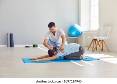 Licensed chiropractor or physiotherapist helping young woman do relaxing forward bending medical exercise on sports mat on floor of physio room, curing back problems, providing professional treatment - Powered by Shutterstock