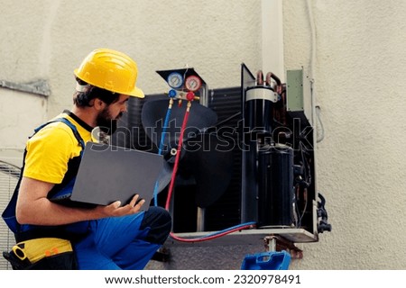 Licensed technician commissioned for outside hvac system annual maintenance, looking for refrigerant leaks. Certified expert doing air conditioner inspection, imputing data on laptop
