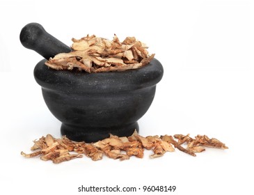 Licorice Root Used In Traditional Chinese Herbal Medicine In A Black Granite Mortar With Pestle Isolated Over White Background. Gan Cao.