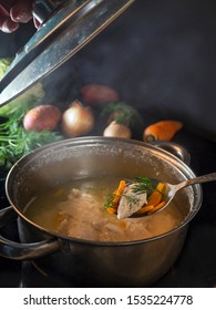 The lid was removed from the saucepan to try the meat hot soup. Steam rises over the soup. On the table are fresh vegetables
