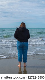 Lido Di Camaiore, Italy - November 2 2018: Girl Looking At The Sea In A Cloudy And Cold Day In Winter. She Is Bare Feet Standing On The Beach. 