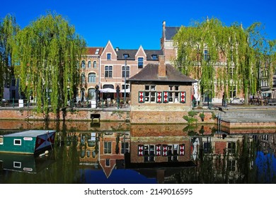 Lier, Belgium - April 9. 2022: View over town moat on old medieval buildings, ancient eel fishing boat, quay with waterfront restaurant, green trees, clear blue sky 