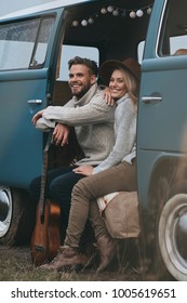 Life Is An Adventure.  Beautiful Young Couple Looking Away And Smiling While Sitting In Blue Retro Style Mini Van