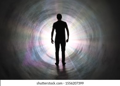 Life after death concept. Silhouette of man's soul is walking to bright light - rays of god inside tunnel.