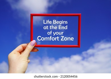 Life begins at the end of your Comfort Zone. Red frame in a female hand against the blue sky. Go beyond thinking. Motivational concept