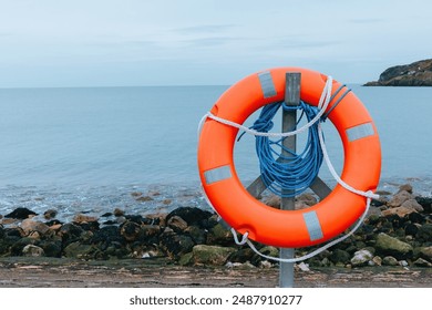 Life buoy is mounted on a post by a rocky shore, overlooking a calm sea, water safety - Powered by Shutterstock