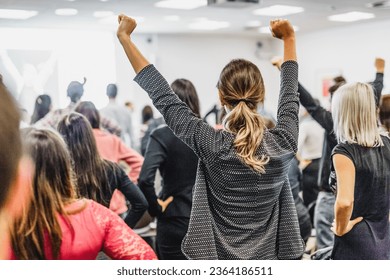 Life coaching symposium. Speaker giving interactive motivational speech at business workshop. Rear view of unrecognizable participants feeling empowered and motivated, hands raised high in air. - Shutterstock ID 2364186511