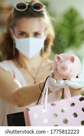 Life During Coronavirus Pandemic. Closeup On Female Shopper With Medical Mask, Piggy Bank, White Rubber Gloves And Paper Shopping Bags.