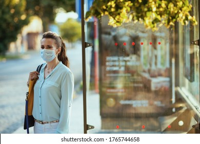 Life during coronavirus pandemic. modern 40 years old woman in blue blouse with medical mask waiting for transport at the bus stop outdoors on the city street.