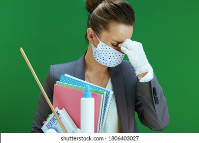 Life During Covid-19 Pandemic. Stressed Modern Teacher Woman In White Blouse With Medical Mask, Rubber Gloves, Textbook And An Antibacterial Agent Against Chalkboard Green Background.