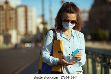 Life during covid-19 pandemic. trendy woman in blue blouse with medical mask, sunglasses and handbag disinfecting hands with an antibacterial agent outdoors on the city street. - Powered by Shutterstock