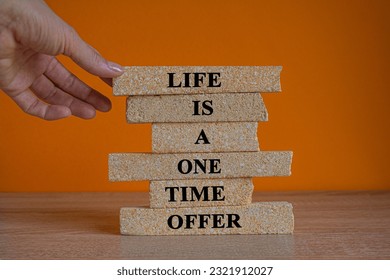 Life is a one time offer. Use it well. Words on a brick locks on a beautiful wooden table, orange background. Businessman hand. Business concept.