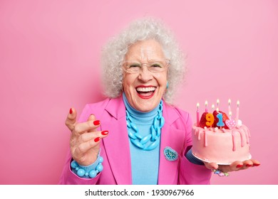 Life only starts when get older. Amused fashionable senior lady celebrates birthday holds cake with burning candles wears makeup isolated over pink background. Positive granny celebrates 91st bday - Powered by Shutterstock