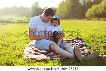 Life portrait of father and son sitting together on the grass in summer evening sunset, dad and child resting on the plaid