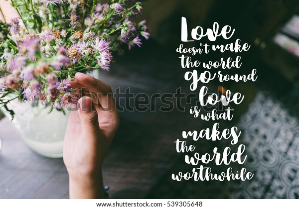 Life quote. Motivation quote\
on soft background. The hand touching purple flowers. Love does not\
make the world go round love is what makes the ride\
worthwhile.