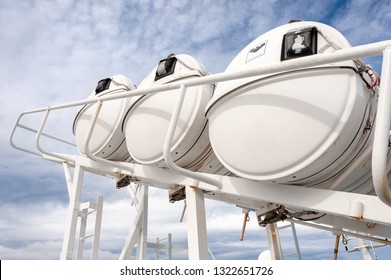 Life rafts on board a passenger ferry. Upwards view of three lifeboat capsules against a blue cloudy sky background