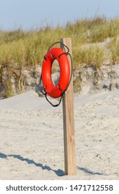 Life saving orange ring float on a wooden post on the beach in front of the green sand dunes
