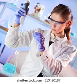 Life Scientists Researching In Laboratory. Focused Female Life Science Professional Pipetting Blue Solution Into Glass Cuvette. Lens Focus On Researcher's Eyes. Healthcare And Biotechnology Concept.