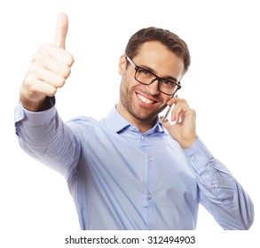 Life Style, Business  And People Concept: Casual Young Man Showing Thumbs Up Sign, While Speaking On The Phone And Smiling To The Camera. Isolated On White Background