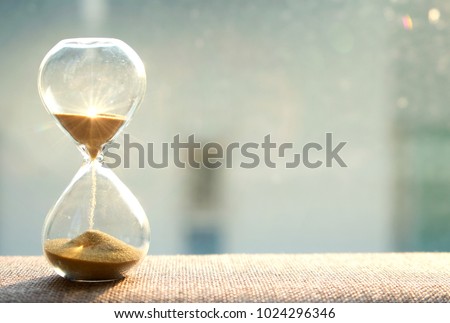 Life time passing concept. Hourglass with sun light background