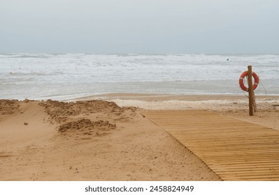 Lifebuoy on a wooden post next to the beach access on a stormy and windy day as the coast is hit by a heavy waves from the sea. - Powered by Shutterstock