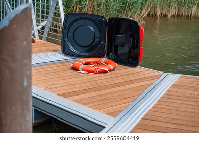 Lifebuoy ring resting near the open safety case on a wooden dock, providing vital equipment for water rescue and safety preparedness by the scenic waterway in an emergency situation. - Powered by Shutterstock