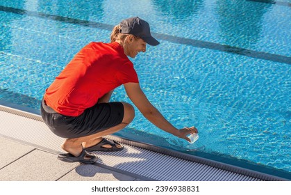 Lifeguard crouching by swimming pool collecting water sample in a clear container in a hotel - Powered by Shutterstock