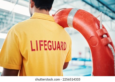 Lifeguard, man and swimming pool safety at indoor facility for training, swim and exercise. Pool, attendant and water sports worker watching for danger, protection or diving athletics, ready and safe