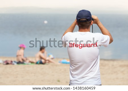 Lifeguard on the beach looking through binoculars. Safety while swimming.