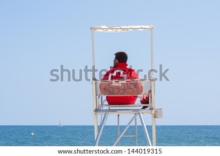 A lifeguard sitting on surveillance tower, front of the sea. / Lifeguard
