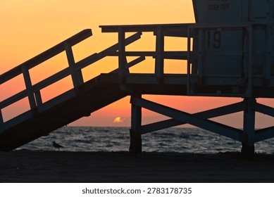 Lifeguard Tower 19 frames the setting sun over the ocean in Hermosa Beach, California.