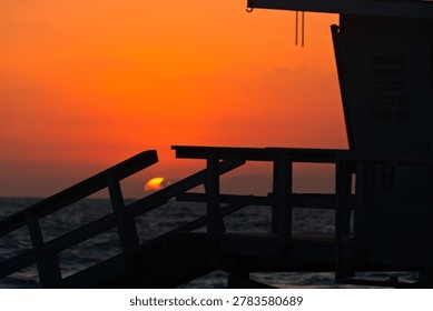 Lifeguard Tower 19 frames the setting sun over the ocean in Hermosa Beach, California.