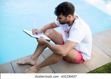 Lifeguard writing on clipboard at poolside on a sunny day - Powered by Shutterstock