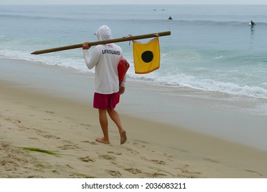 lifeguard with yellow flag and floatation device walking on beach