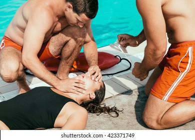 Lifeguards in training, doing CPR procedure with victim. One lifeguard checking air passages, other preparing rescue mask - Powered by Shutterstock