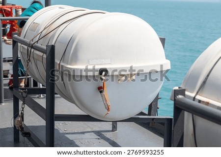 Liferaft Container on Ferry Deck at Sea. Liferaft container secured on a ferry deck with a metal frame and ropes, set against calm turquoise sea, highlighting marine safety equipment and maritime transport environment.