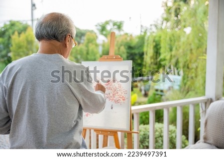 Lifestyle artist. Senior old man painting picture artwork using brush and water color on canvas, portrait elderly white haired paint at his easel outside green nature, Happy retirement and activity