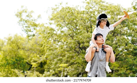 Lifestyle Asian family Father and son sat on his shoulders and run in  park. Paper plane as a toy in hand of kid And there are many big trees in garden Is natural in the morning of summer - Shutterstock ID 2177974709