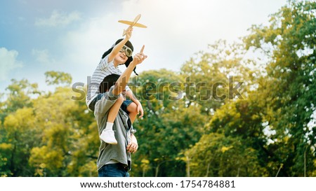 Lifestyle Asian family Father and son sat on his shoulders and run in  park. Paper plane as a toy in hand of kid And there are many big trees in garden Is natural in the morning of summer