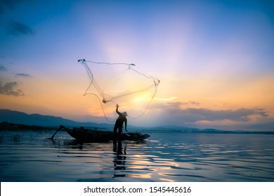 Lifestyle of Asian fisherman on wooden boat for catching freshwater fish in reservoir in the early morning before sunrise - Powered by Shutterstock