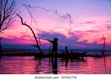 Lifestyle Of Asian Fisherman On Wooden Boat   For Catching Freshwater Fish In Reservoir In The  Early Morning Before Sunrise