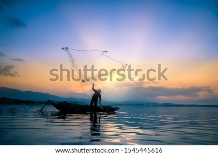 Lifestyle of Asian fisherman on wooden boat for catching freshwater fish in reservoir in the early morning before sunrise