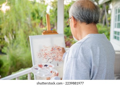 Lifestyle Asian senior old man painting picture artwork using brush and oil color on canvas, elderly people smile paint at his easel outside green nature background, Happy retirement artist activity - Powered by Shutterstock