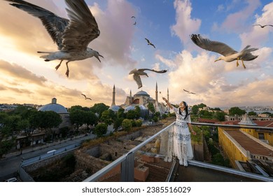 Lifestyle Asian woman tourist feeding seagulls at view point in vacation. There is a Hagia Sophia or Ayasofya Mosque in background. Popular tourist destination. Sultanahmet, Istanbul, Turkiye, Turkey
