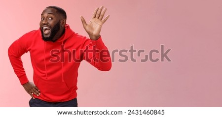 Lifestyle. Attractive funny african american gay beard in red hoodie raise palm waving hello hi howdy gesture acting feminine cute fool around welcoming guests greeting standing pink background.