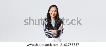Lifestyle, beauty and fashion, people emotions concept. Cheerful cute and shy asian girl cross arms chest modest pose, looking away as laughing and smiling silly, stand white background