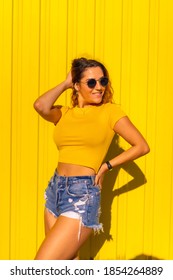 Lifestyle, Caucasian Blonde Girl In Yellow T-shirts And Short Jeans On A Yellow Background. Fashionable Posing With A Smile, Street Photography