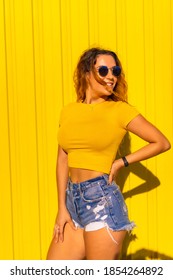 Lifestyle, Caucasian Blonde Girl In Yellow T-shirts And Short Jeans On A Yellow Background. Fashionable Posing With A Smile, Street Photography